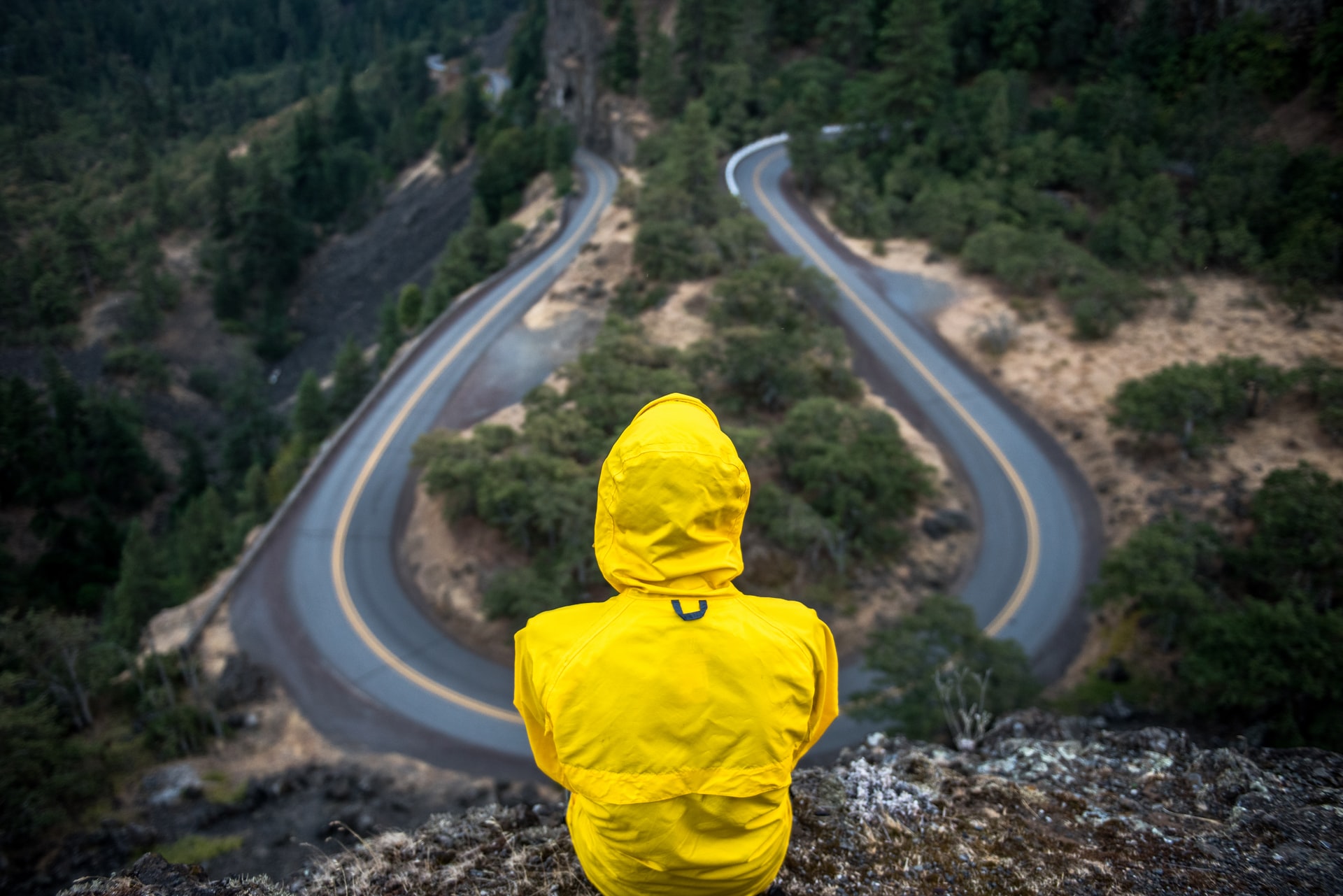 Person sitting on a hill looking at a curvy mountain road