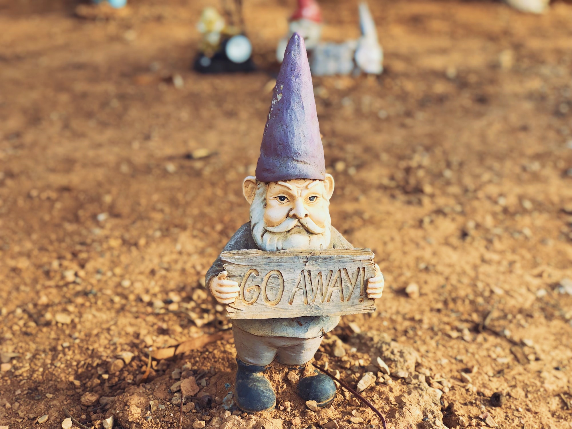 A small garden gnome holding a sign that says "go away!".