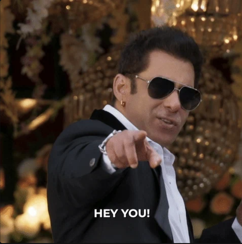 Man in a suit and aviator-styled sunglasses smiling and pointing finger at the viewer and text label "Hey you"